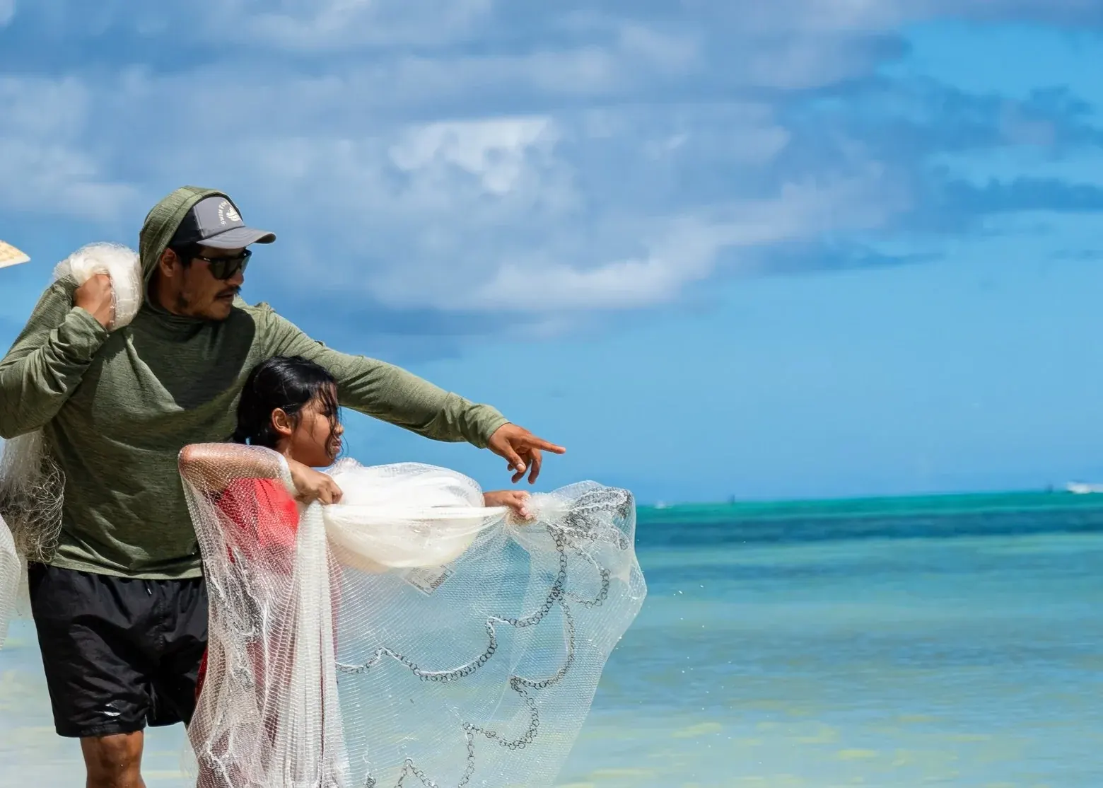 A Talaya Club instructor and a young girl hold a talåya net together at the shoreline, ready to cast