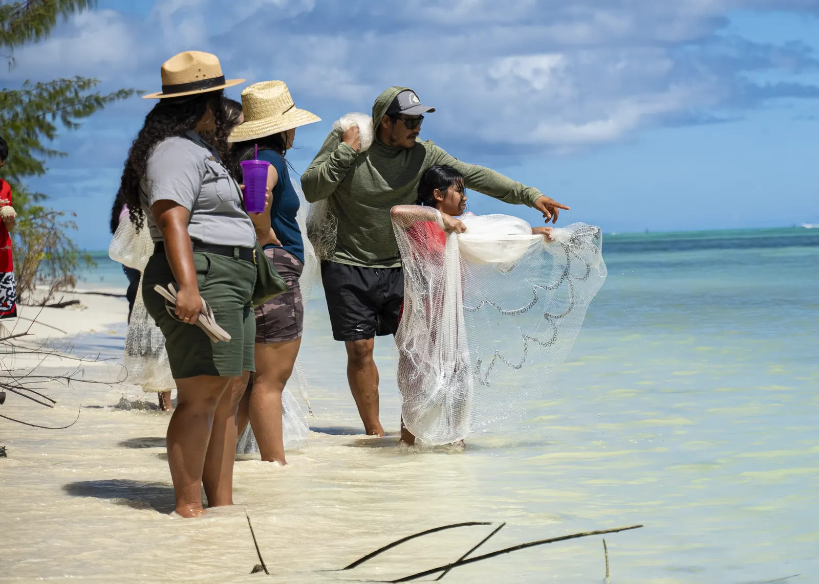 Instructor guiding two young people as they cast a talåya net in shallow water